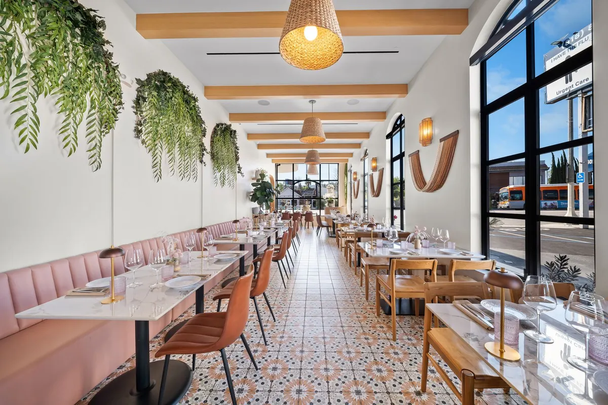 Bright dining room at POPULAR Encino with pink banquette seating, hanging greenery and patterned tile floors